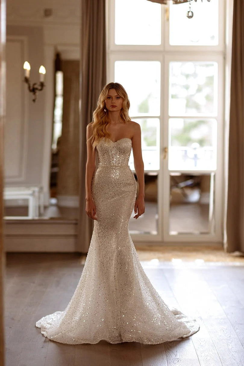 This Marcela Dress features stunning sequins adorning the entire mermaid-style silhouette, making it the perfect choice for a glamorous wedding look. The intricate detailing and form-fitting design will highlight your curves, while the sparkling embellishments add a touch of luxury. Make a statement on your special day with this gorgeous dress.