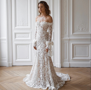 Elevate your special day with the Robe Alana. This exquisite lace mermaid wedding dress boasts an off the shoulder sweetheart neckline and detachable sleeves for an elegant, customizable look. Its long silhouette is designed to stun and captivate, making you feel like a true work of art.