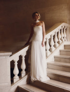 Embody modern elegance on your big day with the Yolanda Gown. Made for the fashion-forward bride, this sleek and minimalistic gown features a tailored bell-shaped bodice and a soft, romantic silk tulle skirt and scarf. The Italian duchess fabric and built-in corset provide a smooth, flattering fit, while the flowing layers of silk tulle add stunning movement.