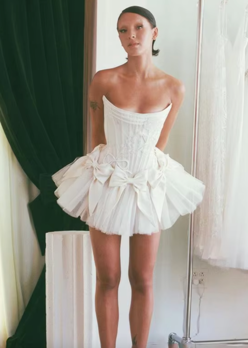 Elevate your style with the Tiara Mini Dress! Crafted with luxurious off-white silk double-faced satin, this dress features a playful mini bow skirt and a delicate corset. Complete your look with the tulle tutu for a touch of elegance and charm. Perfect for any occasion, make a statement with this must-have dress!