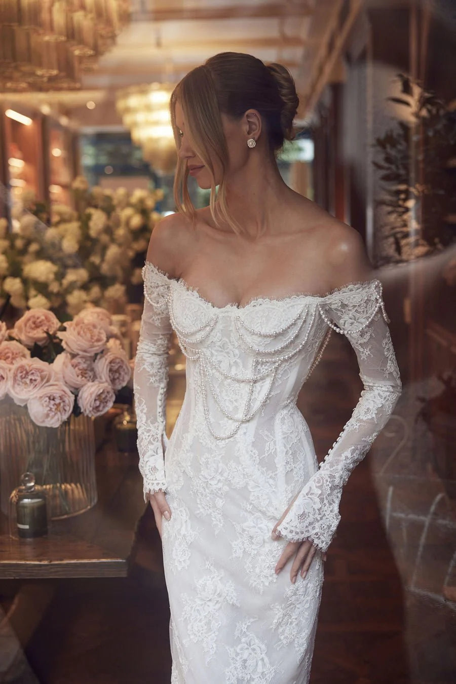 The Caprice Gown exudes royal elegance with its scalloped lace bodice, adorned with pearls and delicate lace sleeves that grace the hands. The unique scalloped detail extends to the hem and train, adding a touch of cascading beauty. Perfect for a regal and sophisticated look on any special occasion.