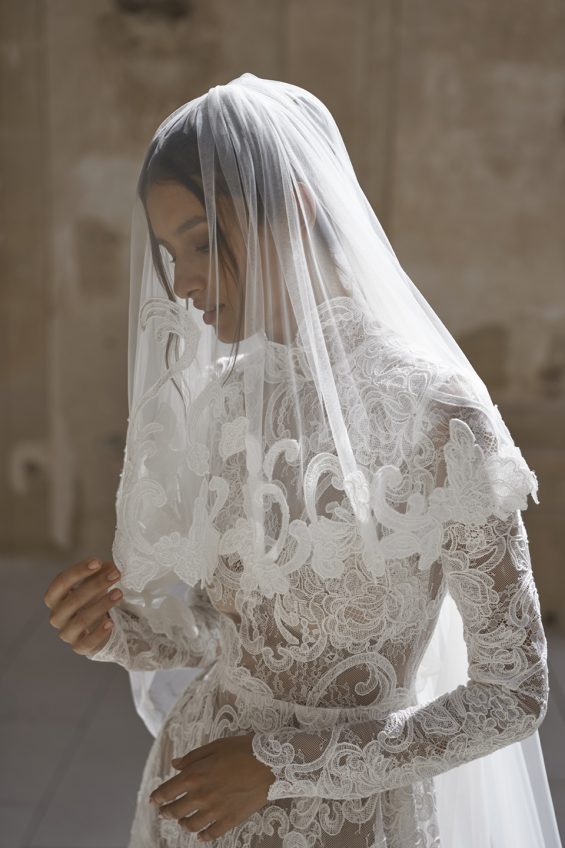 This elegant lace gown will make you feel sophisticated and romantic on your special day. With long sleeves and a ruffle neck, this dress exudes timeless charm. The high slit skirt adds a touch of modernity, while the optional chapel-length veil with matching lace details completes the look.