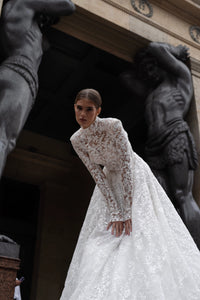 The Lidia Gown is the perfect wedding dress for the modern bride. With a flattering A-line silhouette, elegant long sleeves, and a high collar neckline, this gown is made from delicate lace and embellished with stunning sequins. Make a statement on your special day with this one-of-a-kind gown.