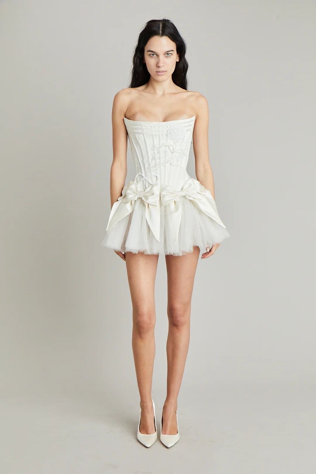 Elevate your style with the Tiara Mini Dress! Crafted with luxurious off-white silk double-faced satin, this dress features a playful mini bow skirt and a delicate corset. Complete your look with the tulle tutu for a touch of elegance and charm. Perfect for any occasion, make a statement with this must-have dress!