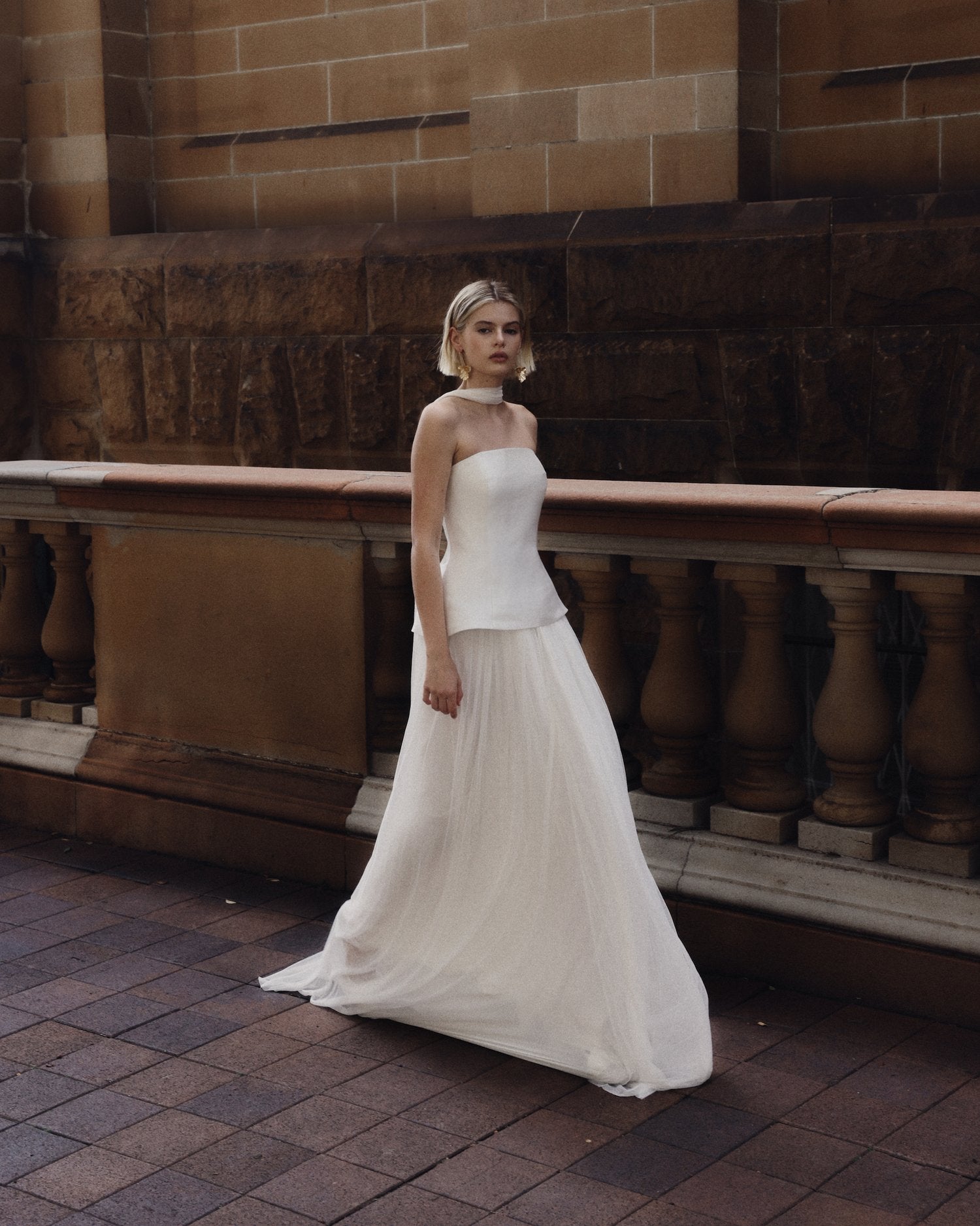 Embody modern elegance on your big day with the Yolanda Gown. Made for the fashion-forward bride, this sleek and minimalistic gown features a tailored bell-shaped bodice and a soft, romantic silk tulle skirt and scarf. The Italian duchess fabric and built-in corset provide a smooth, flattering fit, while the flowing layers of silk tulle add stunning movement.