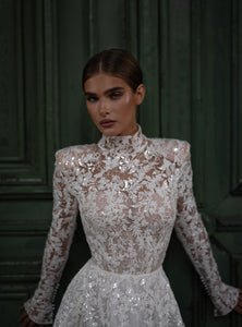 The Lidia Gown is the perfect wedding dress for the modern bride. With a flattering A-line silhouette, elegant long sleeves, and a high collar neckline, this gown is made from delicate lace and embellished with stunning sequins. Make a statement on your special day with this one-of-a-kind gown.