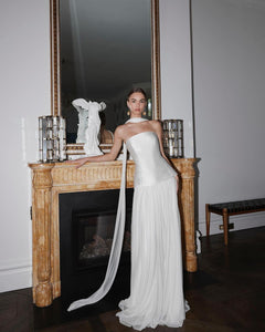 Embody modern elegance on your big day with the Yolanda Gown. Made for the fashion-forward bride, this sleek and minimalistic gown features a tailored bell-shaped bodice and a soft, romantic silk tulle skirt and scarf. The Italian duchess fabric and built-in corset provide a smooth, flattering fit, while the flowing layers of silk tulle add stunning movement.