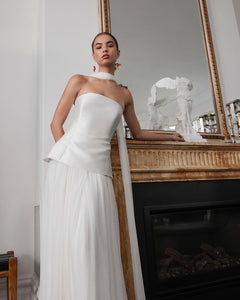 Embody modern elegance on your big day with the Yolanda Gown. Made for the fashion-forward bride, this sleek and minimalistic gown features a tailored bell-shaped bodice and a soft, romantic silk tulle skirt and scarf. The Italian duchess fabric and built-in corset provide a smooth, flattering fit, while the flowing layers of silk tulle add stunning movement.