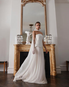 Embody modern elegance on your big day with the Yolanda Gown. Made for the fashion-forward bride, this sleek and minimalistic gown features a tailored bell-shaped bodice and a soft, romantic silk tulle skirt and scarf. The Italian duchess fabric and built-in corset provide a smooth, flattering fit, while the flowing layers of silk tulle add stunning movement.