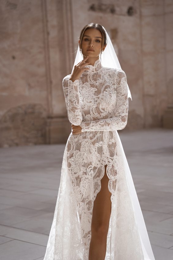 This elegant lace gown will make you feel sophisticated and romantic on your special day. With long sleeves and a ruffle neck, this dress exudes timeless charm. The high slit skirt adds a touch of modernity, while the optional chapel-length veil with matching lace details completes the look.