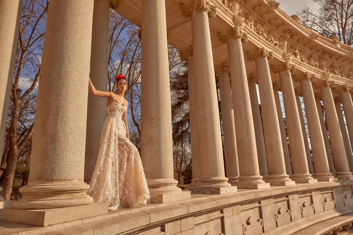 Eleina is the embodiment of opulent bridal elegance—an exquisite garment where each and every stitch, detail, and cut is thoughtfully considered. Drawing inspiration from the fervent emotions of love, desire, and celestial beauty, the scoop neck and goddess-like silhouette effortlessly transitions from the ceremony to the festivities, enhanced by a layered ball gown overskirt that adds depth and texture for a captivating second look. The delicate three-dimensional flower embroidery and petal-adorned straps 