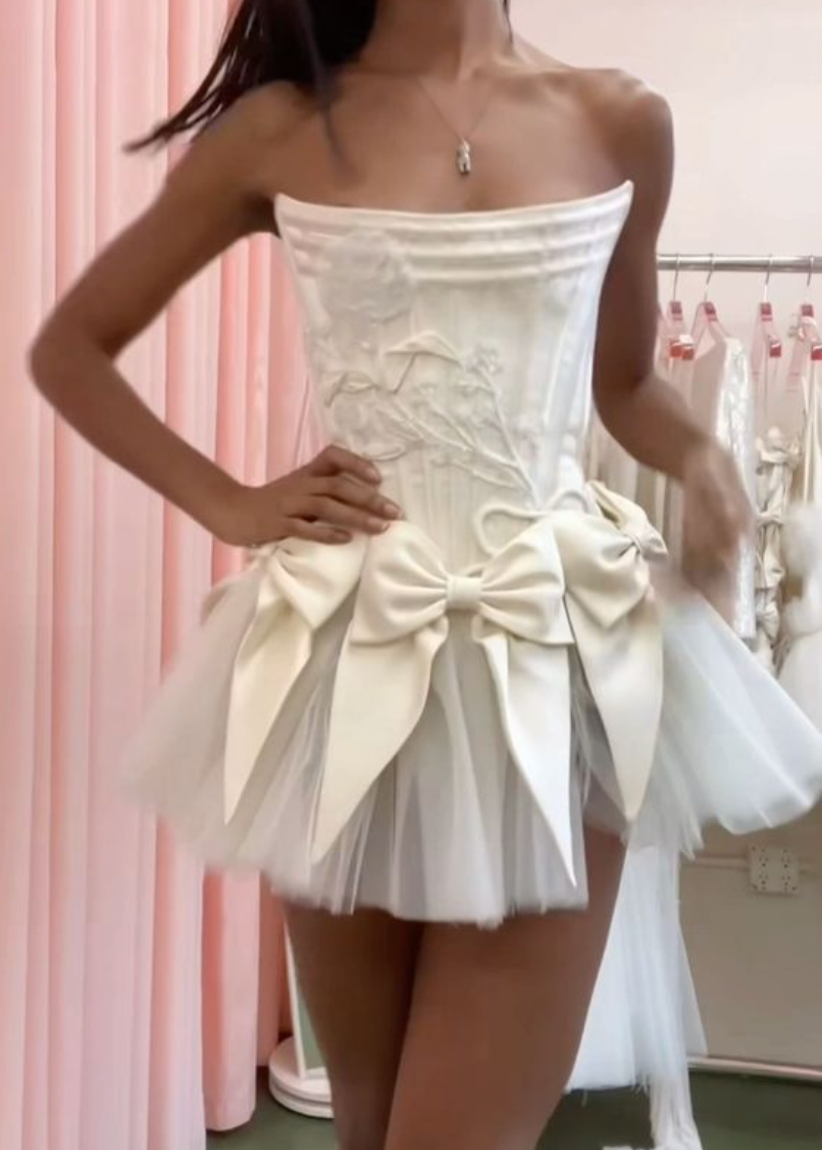 Elevate your style with the Tiara Mini Dress! Crafted with luxurious off-white silk double-faced satin, this dress features a playful mini bow skirt and a delicate corset. Complete your look with the tulle tutu for a touch of elegance and charm. Perfect for any occasion, make a statement with this must-have dress!