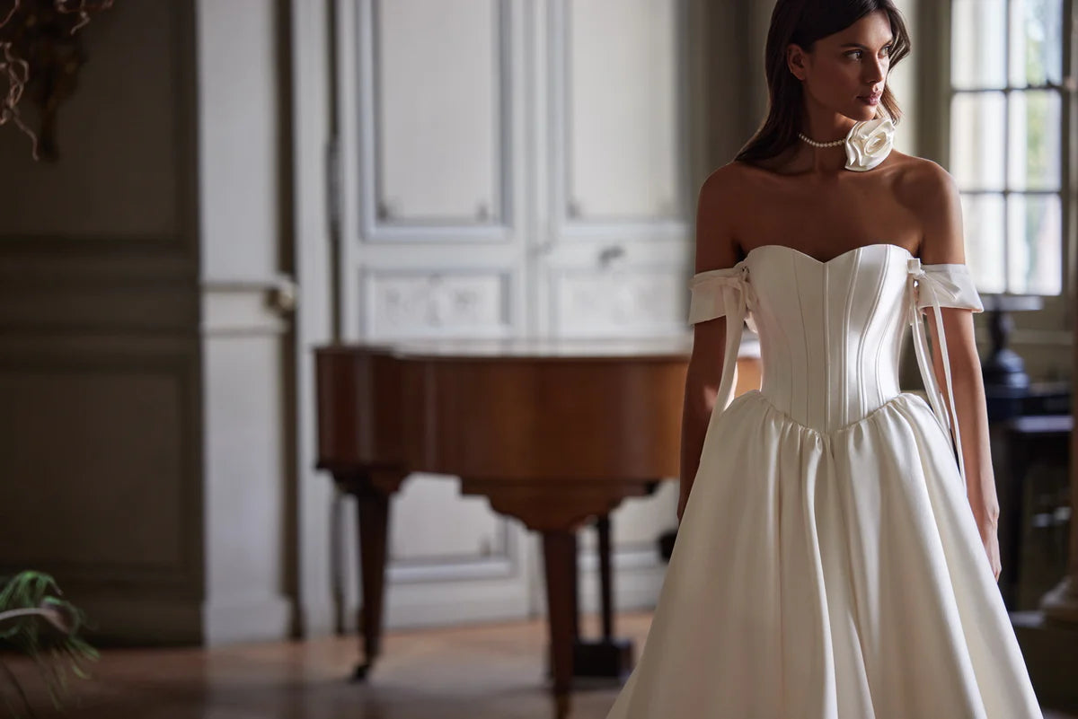 Introducing the Erza Gown - a minimalist wedding dress made with luxurious mikado fabric. The corset design features open shoulders and removable sleeves, tied with elegant bows for a sophisticated touch. Perfect for the modern bride seeking timeless elegance on her special day.