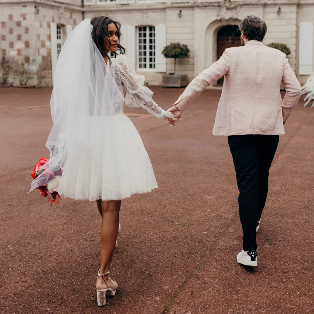 Robe Sidonie is a timeless mini polka dot tulle wedding dress. Featuring a simple V-neck design and an above-knee hem, the dress is finished with ruching details, a low open back, and lantern sleeves. Its classic silhouette is sure to make you the star of your special day.