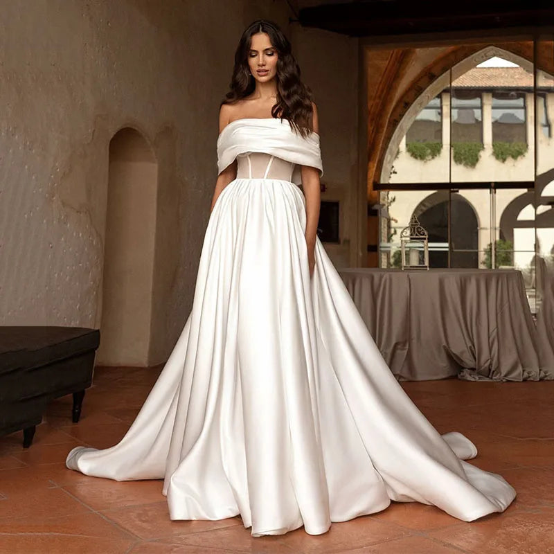 Indulge in luxury with our Robe Satine. This elegant off-the-shoulder satin gown features delicate ruching for a timeless and sophisticated look. Perfect for a stylish and stunning bridal ensemble. Experience the ultimate in bridal fashion with our Robe Satine.