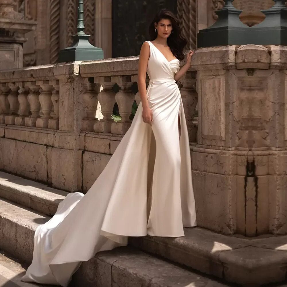 Feel like royalty on your special day in the Robe Bellamy! This stunning wedding dress features a classic V-neckline and sleeveless construction that'll make you look like an absolute dream. The elegant ruched skirt and slit detail is the perfect finishing touch, and you'll be saying "I do" in style!