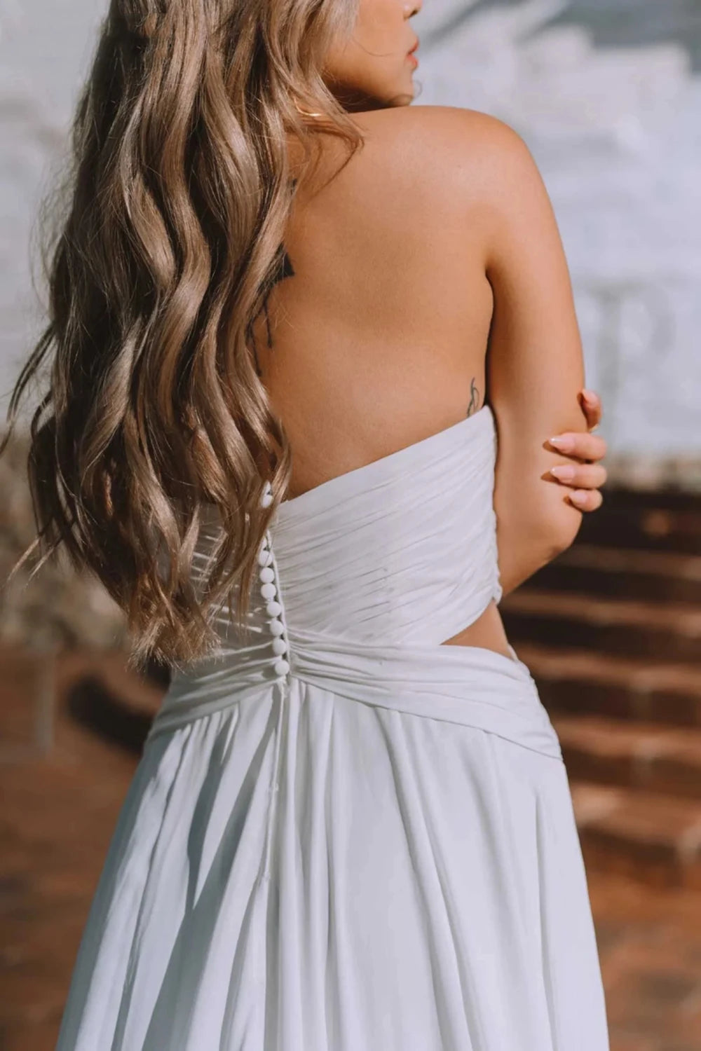 Dare to be different on your special day with the Robe Capucine. This Sirene Boho Off Shoulder Wedding Dress boasts a chic V-neck and stylish chiffon material. The side split, cut out design, and backless look add a touch of uniqueness. Plus, the pleats, button accents, and court train offer a dreamy, ethereal feel.