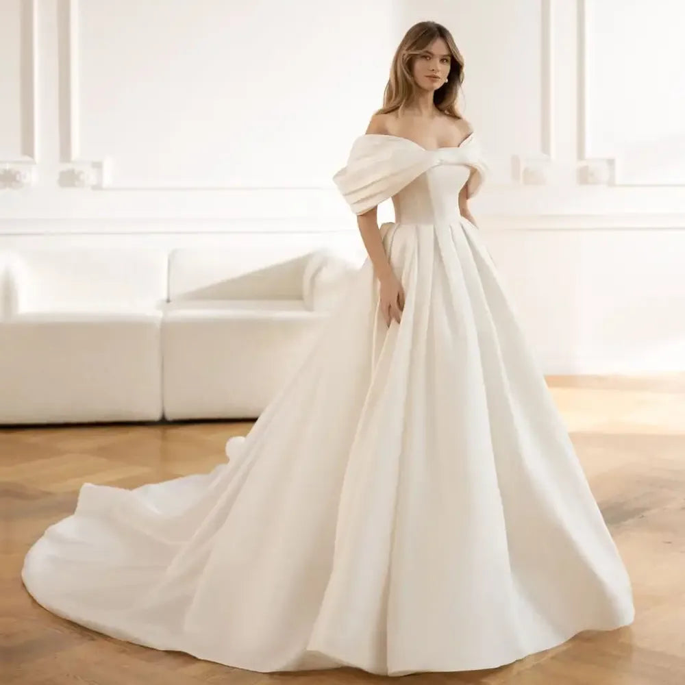 Introducing the Robe Elia - the perfect addition to your special day! This wedding dress features an elegant sweetheart neckline, delicate bow accents, and a romantic off the shoulder design. The A-line silhouette flatters every figure, while the ruched bodice adds a touch of sophistication.