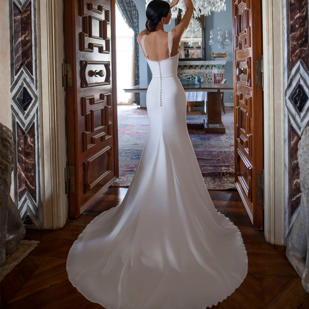 Introducing the exquisite Robe Odetta, the ultimate bridal wedding dress. With a sexy backless design and adorned with delicate pearls, this dress will make you feel like a true goddess on your special day. Make a statement with the elegant neck and stunning trailing gown. A luxurious choice for any sophisticated bride.