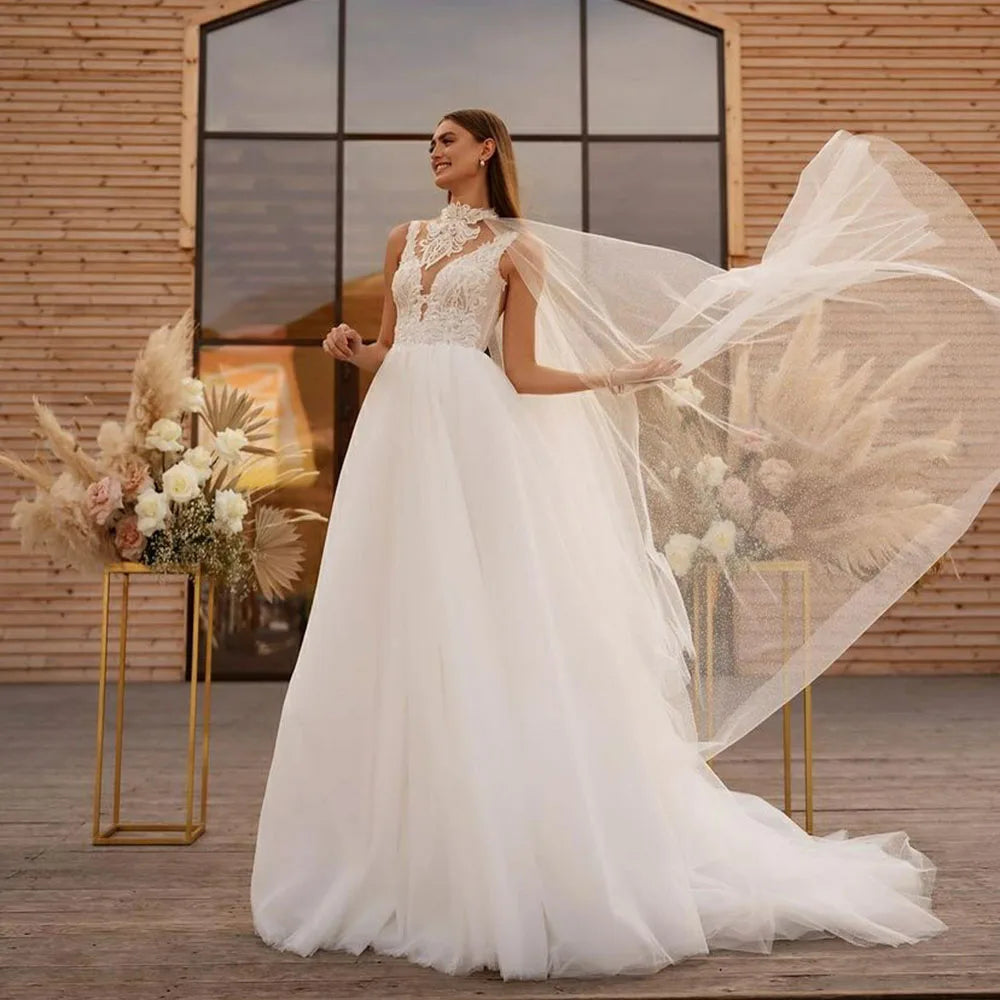 Get ready to say "I do" in style with Robe Claude! This boho wedding dress features a unique cape design, A-line silhouette, and intricate lace and tulle detailing. The high neck and illusion princess bride design will make you feel like royalty on your special day.