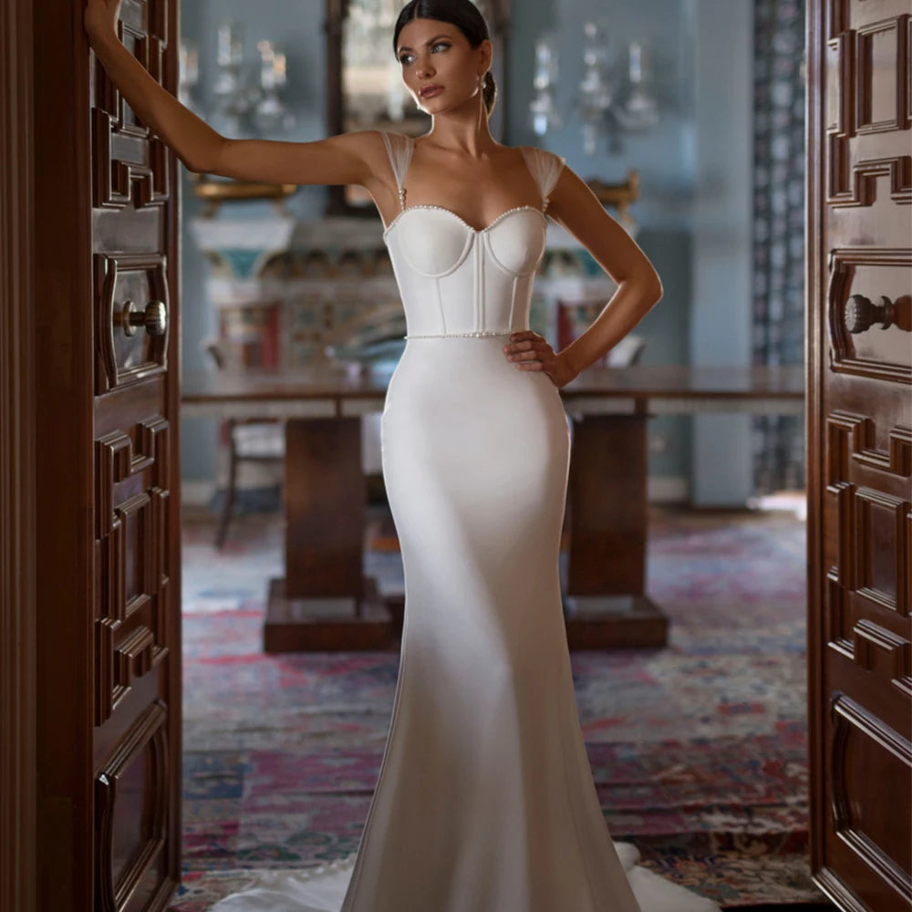 Introducing the exquisite Robe Odetta, the ultimate bridal wedding dress. With a sexy backless design and adorned with delicate pearls, this dress will make you feel like a true goddess on your special day. Make a statement with the elegant neck and stunning trailing gown. A luxurious choice for any sophisticated bride.