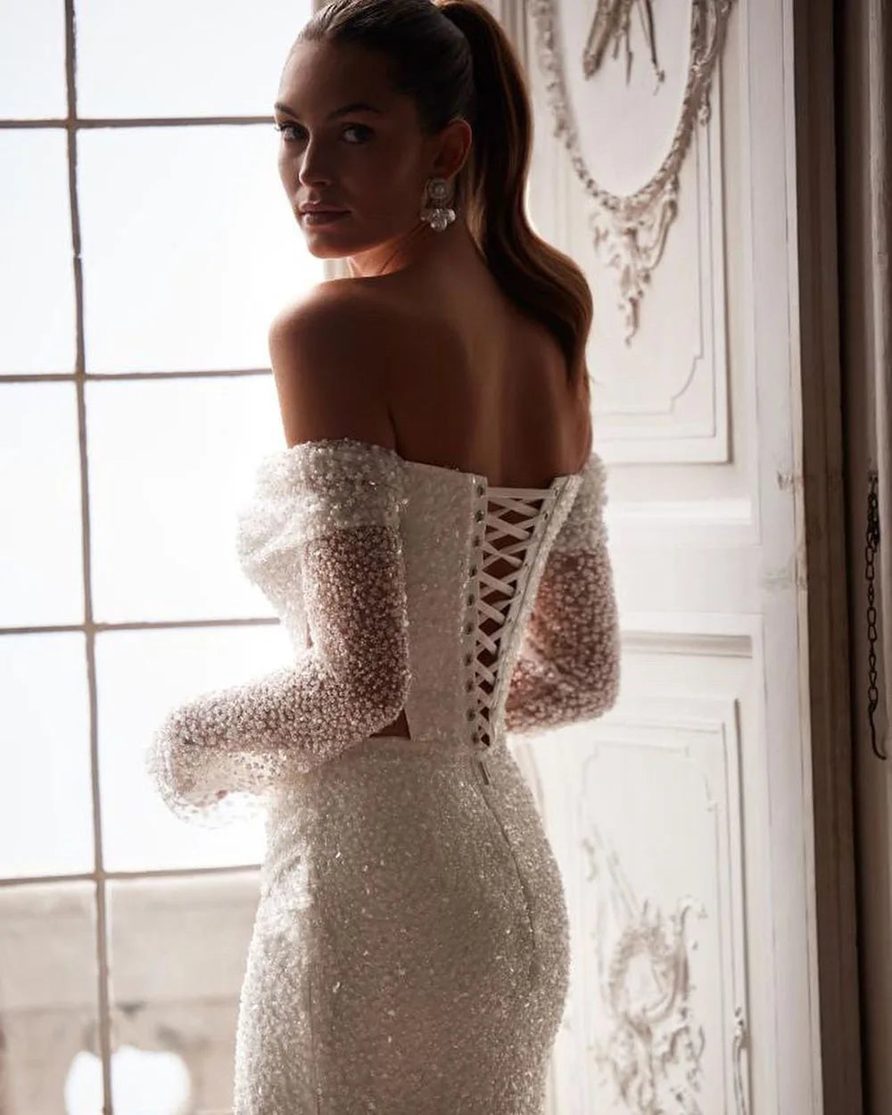 Update your wedding wardrobe with the exquisite Robe Veronique. This enchanting gown features long sleeves and a sexy mermaid silhouette adorned with shimmering glitter sequins. Walk down the aisle in style and make a statement on your special day.