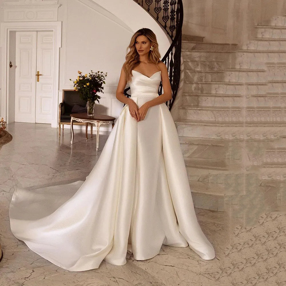 Introducing the elegantly modern Robe Perrine, the perfect wedding dress for the sophisticated bride. With its satin pleats and overskirt, this dress complements your figure and adds a touch of glamour to your special day. Make a statement with this stunning gown.