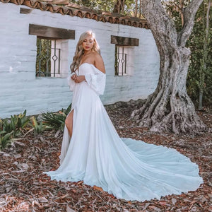 Dare to be different on your special day with the Robe Capucine. This Sirene Boho Off Shoulder Wedding Dress boasts a chic V-neck and stylish chiffon material. The side split, cut out design, and backless look add a touch of uniqueness. Plus, the pleats, button accents, and court train offer a dreamy, ethereal feel.