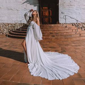 Dare to be different on your special day with the Robe Capucine. This Sirene Boho Off Shoulder Wedding Dress boasts a chic V-neck and stylish chiffon material. The side split, cut out design, and backless look add a touch of uniqueness. Plus, the pleats, button accents, and court train offer a dreamy, ethereal feel.