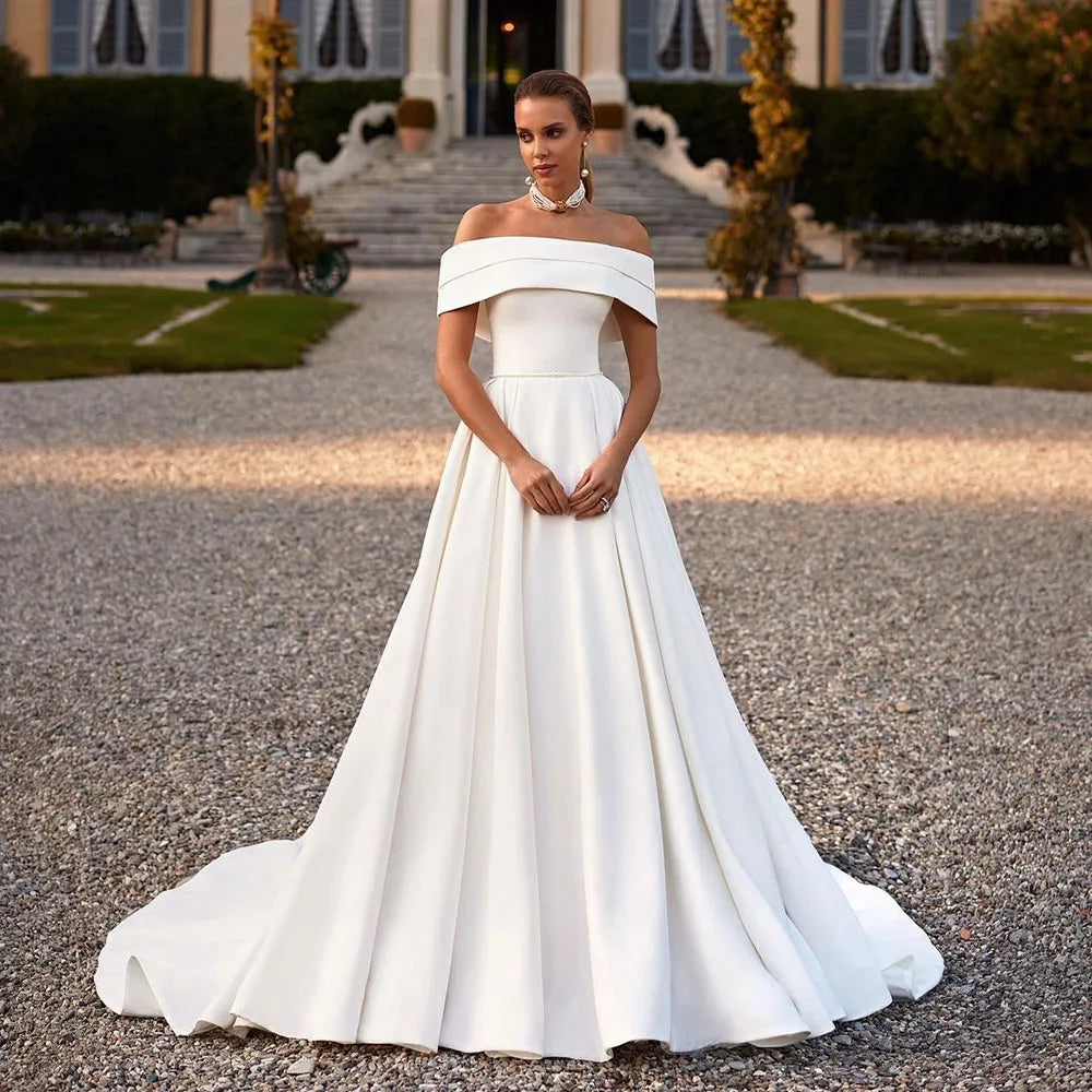 Indulge in luxury on your special day with the Robe Lotta. Featuring an elegant white A-line design and an off-the-shoulder neckline, this wedding dress is made of smooth satin for a sophisticated look and feel. Make a statement that exudes grace and refinement with this exclusive piece.