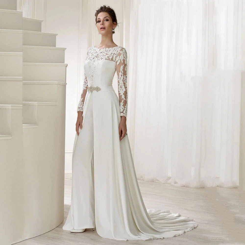 Elegance and versatility combine in our Combinaison Madisson. From the modest long sheer sleeves to the stunning lace detailing, this custom-made jumpsuit is perfect for the modern bride. The detachable skirt train adds a touch of drama, allowing you to seamlessly transition from ceremony to reception.