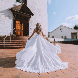 Dare to be different on your special day with the Robe Capucine. This Sirene Boho Off Shoulder Wedding Dress boasts a chic V-neck and stylish chiffon material. The side split, cut out design, and backless look add a touch of uniqueness. Plus, the pleats, button accents, and court train offer a dreamy, ethereal feel.