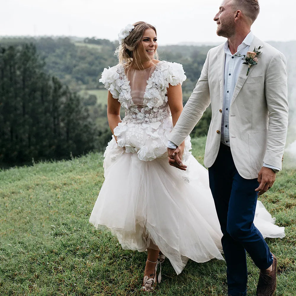 Robe Lorraine is crafted from the finest materials, featuring luxury hand-sewn flowers and a modern backless silhouette. Delicate short sleeves and a puffy tulle skirt turn this rustic ballgown into the ultimate bridal piece. With a deep neckline to flatter the figure, the dress is custom-made to create the perfect fit for the special day.