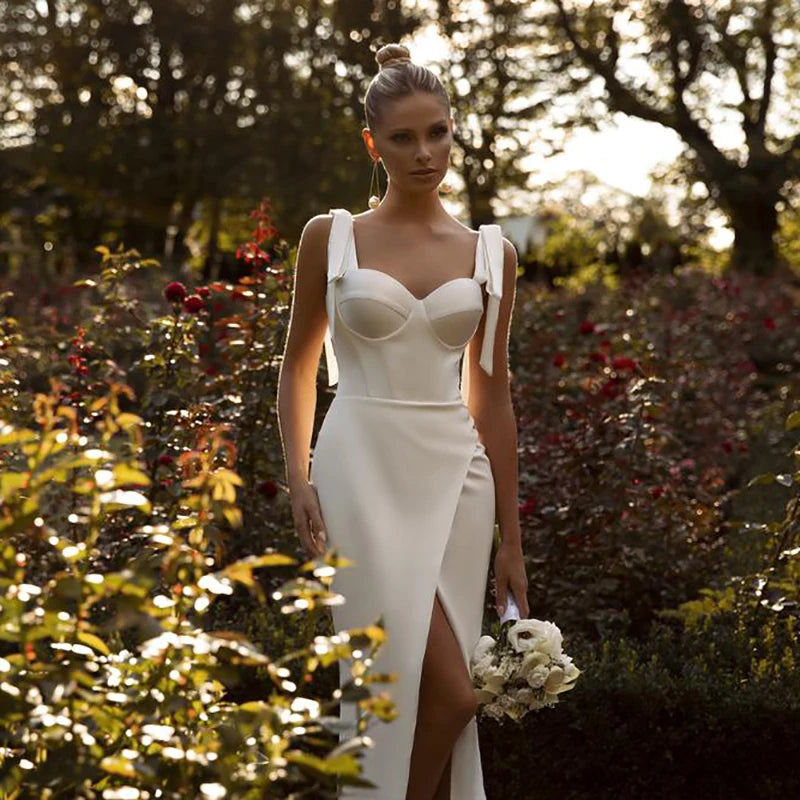 Elevate your wedding day look with our Robe Odalis. The figure-flattering mermaid silhouette is enhanced with delicate bow straps and elegant side split. The addition of white pearls adds a touch of opulence to your bridal ensemble. Make a statement on your special day with this classic yet modern dress.